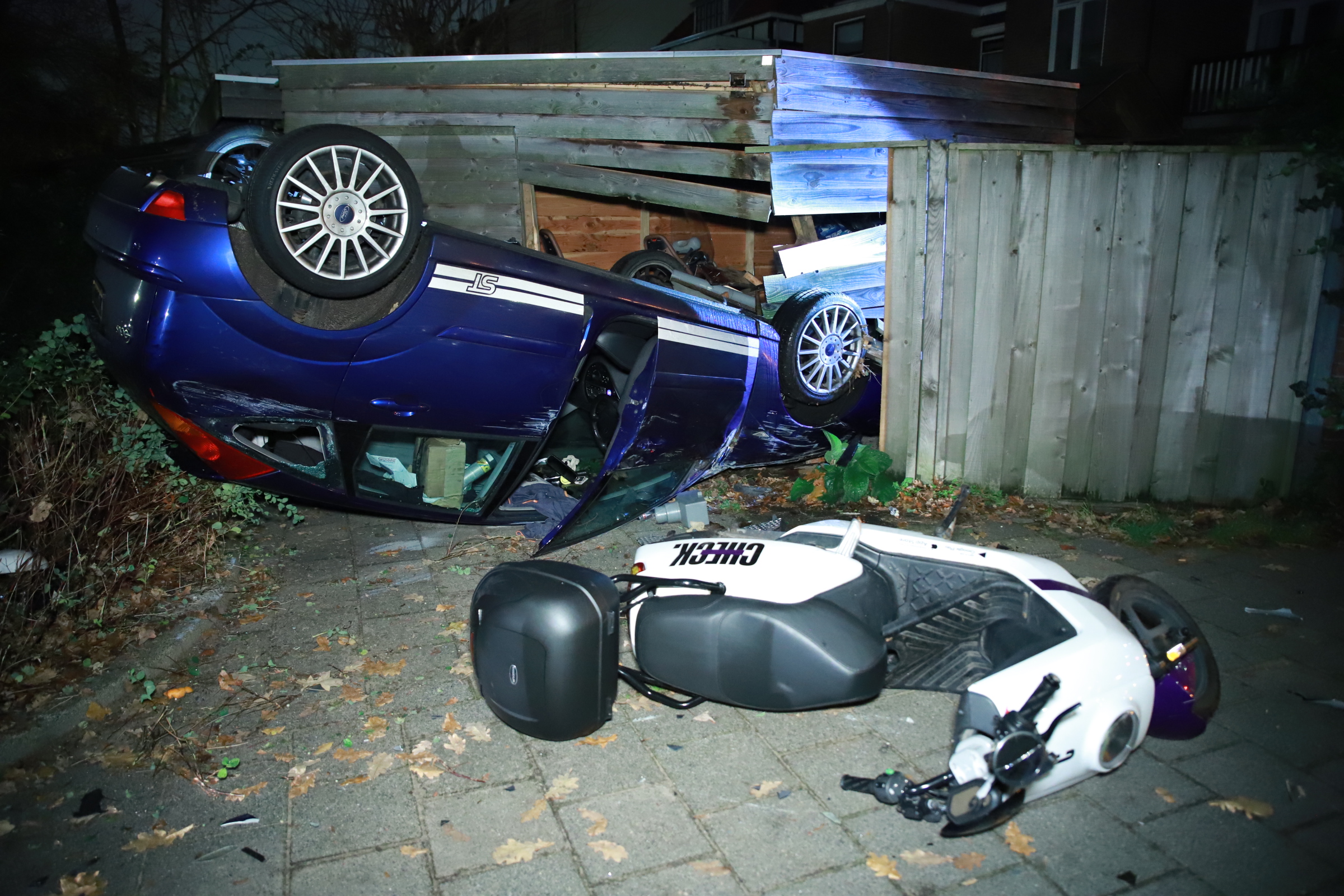 Auto schiet ondersteboven door schutting en schuur heen aan Acacialaan